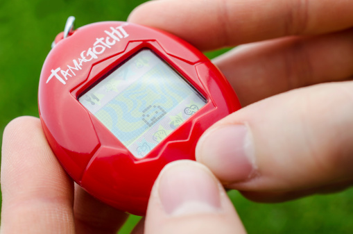 London, England, May 17, 2014: A womain is playing with a Tamagotchi in a garden. Green grass background