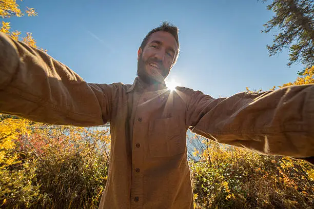 Young cheerful man traveling in Canada takes a selfie portrait by the lake. Autumn season.