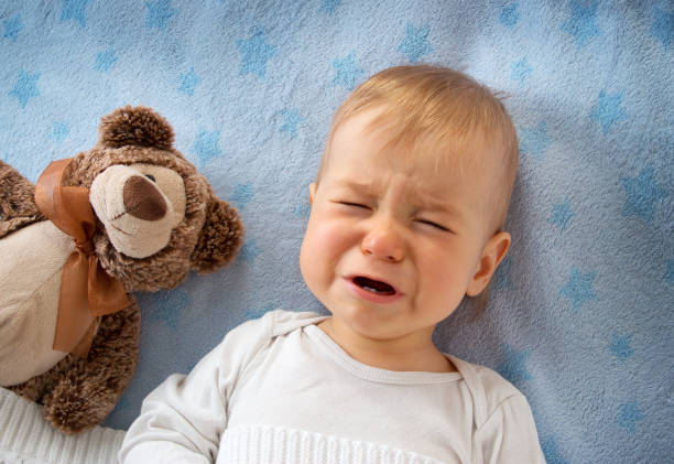 One year old baby crying One year old baby crying in bed with a teddy bear baby sleeping bedding bed stock pictures, royalty-free photos & images