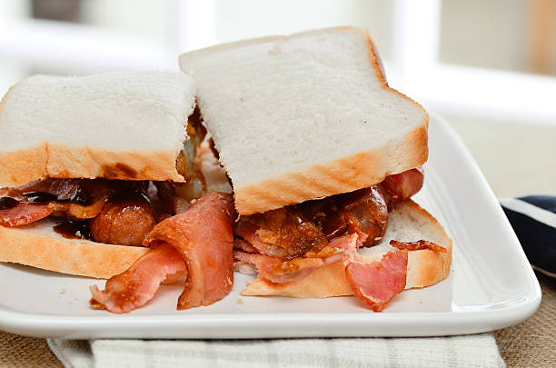 istock Sausage and bacon sarnie with brown sauce on white bread. 492990242