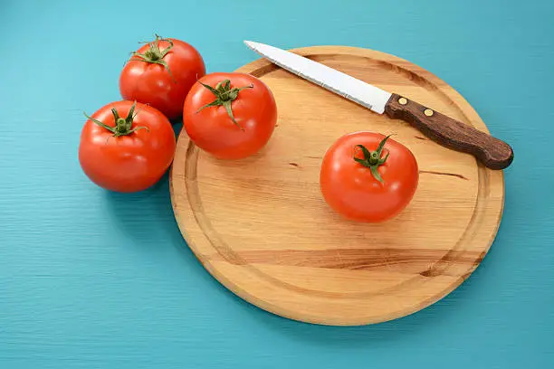 Fresh tomatoes with a serrated kitchen knife on a wooden chopping board