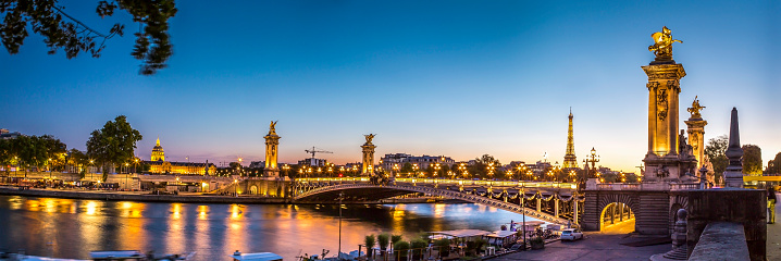 Panoramic view at twilight time of the day of the iconic bridge Alexandre III in the center of Paris in France. In the background, we can also see the Eiffel Tower and Les Invalides monuments.