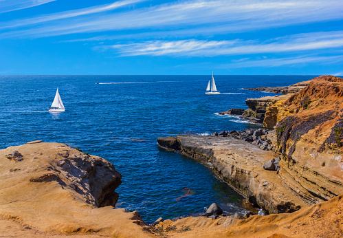 Rocky cove of Point Loma's Sunset Cliff Park fills the foreground leading back to the Pacific Ocean and sailboats, San diego, California