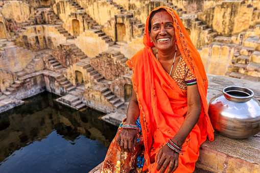 Indian woman resting inside stepwell in village near Jaipur, Rajasthan, India. Women and children often walk long distances to bring back jugs of water that they carry on their head. 