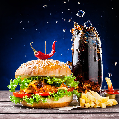 Veggie burger, French fries, ketchup and ice cubes falling in cola glass