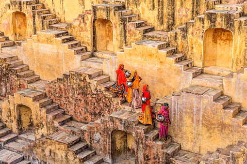 Indian women carrying water from stepwell near Jaipur, Rajasthan, India. Women and children often walk long distances to bring back jugs of water that they carry on their head. 