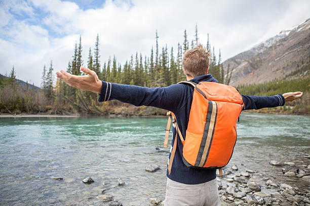 istock Young man by the river arms outstretched for positive emotion 493065668