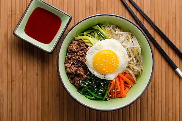 Bibimbap is a classic Korean dish, it's a bowl of rice topped with assorted seasoned vegetables and meat. To finish it off, a fried egg sits on top and a spicy chili sauce can be added.