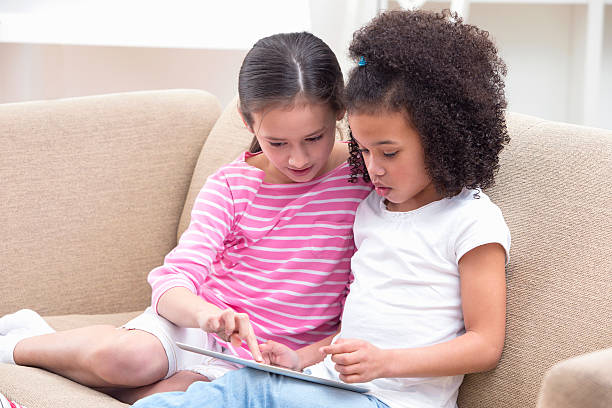 istock Two Girls Sitting On Sofa Using Digital Tablet At Home 493070909