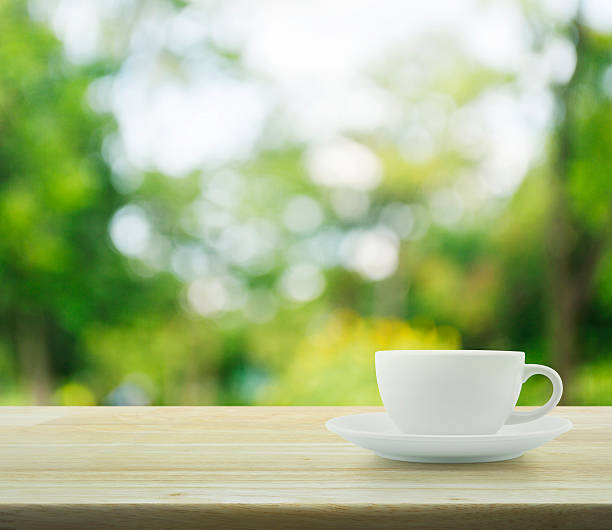 istock White cup on wooden table over tree bokeh background 493078092