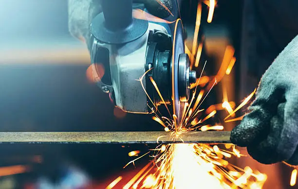 Closeup front view of unrecognizable man cutting thin metal rod with electric grinder. Usual day in a workshop. Sparks flying all over.