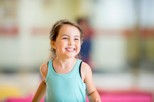A little girl is happily playing in gymnastics class. She is smiling and running across the mat.