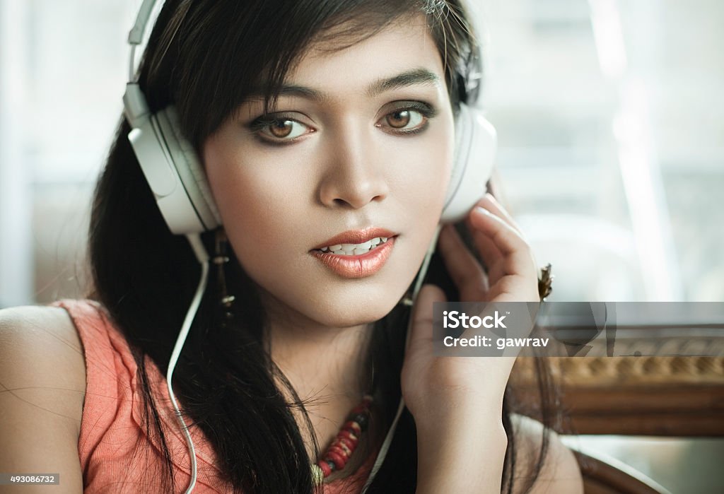 Close-up of teenage Girl listening music through headphones. Indoor, close-up day time image of a beautiful teenage girl listening music through headphones and looking at camera. Horizontal composition with selective focus. 16-17 Years Stock Photo
