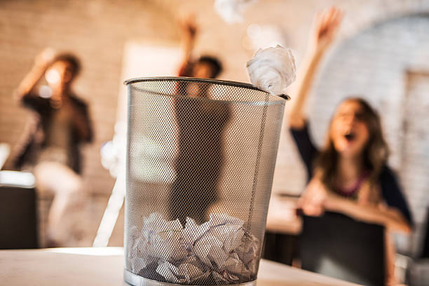 Throwing crumpled paper into a wastepaper basket. Group of people from the background tossing crumpled paper into a garbage can. garbage bin photos stock pictures, royalty-free photos & images