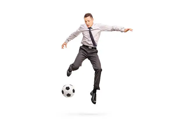 Full length portrait of a young businessperson kicking a football shot in mid-air isolated on white background