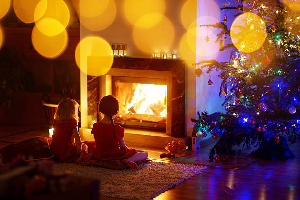 Happy little girls sitting by a fireplace on Christmas eve Happy little girls sitting by a fireplace in a cozy dark living room on Christmas eve young hot stock pictures, royalty-free photos & images