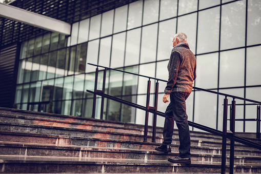 Senior businessman in casual clothing moving up the stairs in front of an office building.