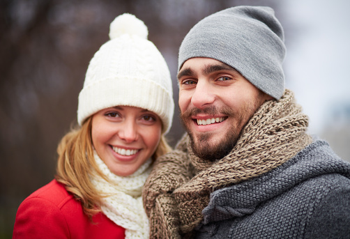 Happy guy and girl in warm clothes looking at camera outside