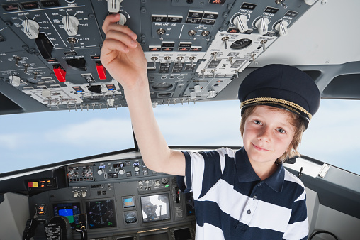 Germany,Bavaria,Munich,boy wearing captain's hat and playing in airplane cockpit