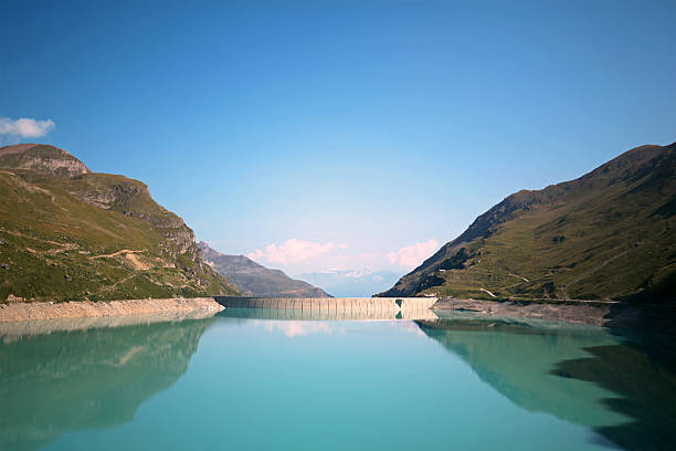 This is a daytime summer landscape image of Lac de Moiry - Moiry Lake Dam - near Grimmentz in Val d'Anniviers Switzerland. Reflections of the surrounding mountains can be seen in the water of the lake.