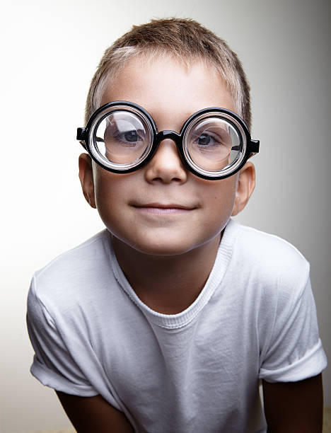 Cute little boy with glasses and white tshirt smiling on the white wall background 