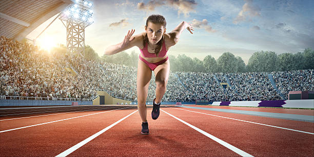 Female athlete sprinting A woman athlete sprinting on the track on the . stadium. The bleachers are full of spectators. The sky is blue and cloudy. The woman is wearing an unbranded bra top with small bottoms and track shoes. all weather running track stock pictures, royalty-free photos & images