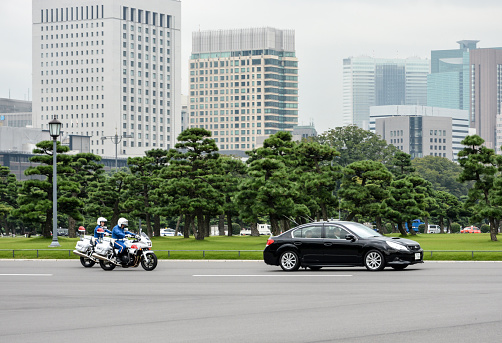 Tokyo, Japan - October 1, 2015: A black car is flanked by two police outriders in a small motorcade in Tokyo city centre.