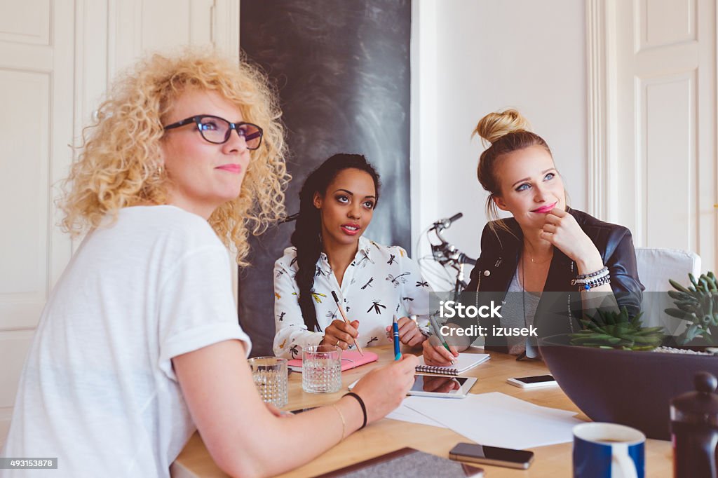 Multi ethnic women team brainstorming Start-up or advertising agency. Multi ethnic women team of designers - caucasian and afro american - meeting in an office, sitting at the table and brainstorming. 2015 Stock Photo