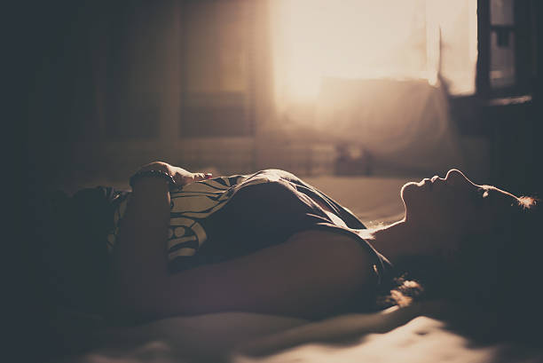 Sad girl lying in bed Sad girl in bed, backlit scene. Desaturated image. only women women bedroom bed stock pictures, royalty-free photos & images