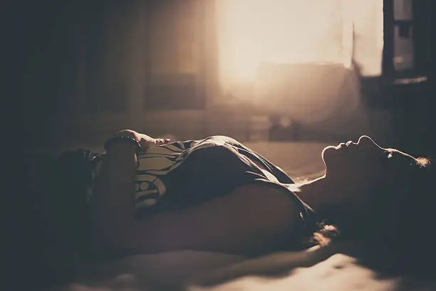 Sad girl in bed, backlit scene. Desaturated image.