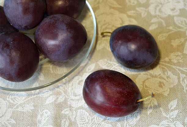 istock Plums on the transparent saucer on tablecloth with white roses 493156406