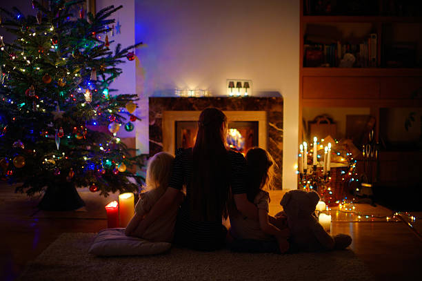 istock Young mother and daughters sitting by a fireplace on Christmas 493162806