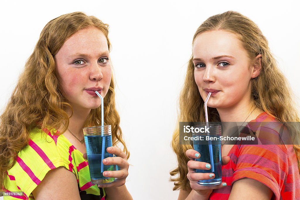 Two teenagers drink blue soda Two caucasian teenage girls drink blue soft drinks sucking through straws. The filled glasses are being hold in a hand in front of the shoulder. Both dutch girls with long hair smile and look at the camera. Isolated on white background.  Soda Stock Photo