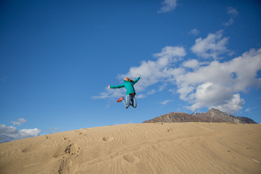Young cheerful woman in desert jumping high up in the air. She is enjoying nature. 