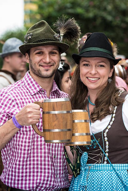 Blumenau, Santa Catarina, Brasil - October 17, 2015: A close-up of a couple, dressed in German costume cheering with wooden beer mugs on the street parade in the heart of Blumenau to celebrate the Oktoberfest, along with people in the background.