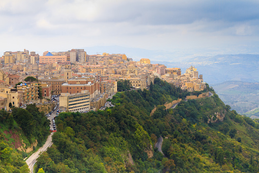 Panoramic view of downtown Enna Sicily perched high on a green hill under an overcast sky. Copy space available in the sky.