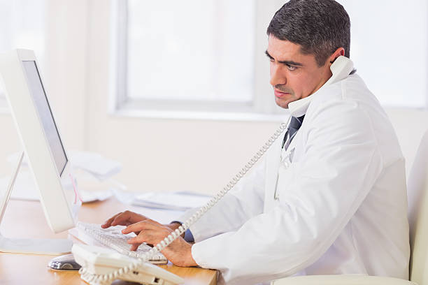 istock Concentrated male doctor using computer and phone 493201009