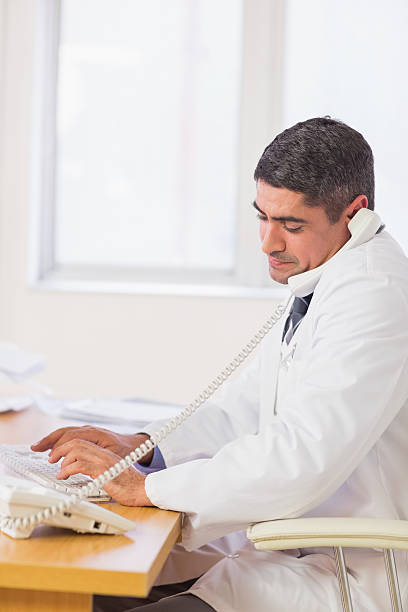 istock Concentrated male doctor using computer and phone 493201011