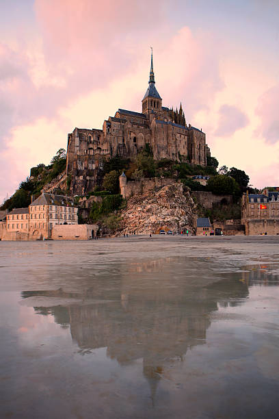 Beautiful view of the famous Le Mont Saint Michel. East across the tidal bay from the salt marsh at a beautiful early morning colorful cloudy sunrise time in Normandy, Northern France