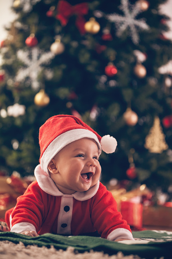 Cute baby luying down on the floor near Christmas tree.