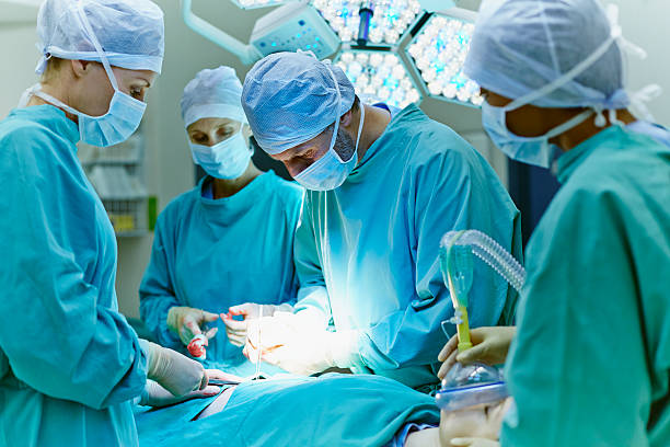surgeons performing surgery in operating room - cirujano fotografías e imágenes de stock