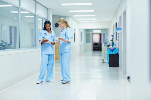 Full length of female nurses discussing medical documents in hospital corridor