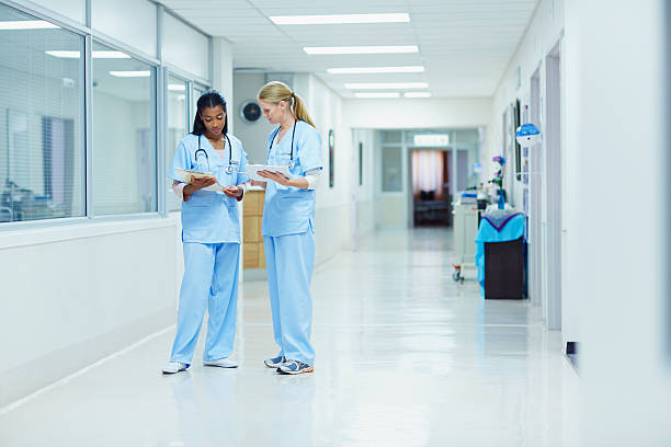 Nurses discussing medical documents in hospital Full length of female nurses discussing medical documents in hospital corridor medical building stock pictures, royalty-free photos & images