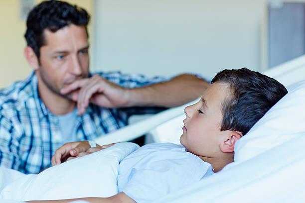 Tensed father with ill son sleeping in hospital Tensed father looking at ill son sleeping in bed at hospital ward sick child hospital bed stock pictures, royalty-free photos & images