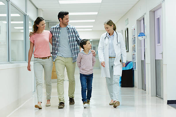 Doctor walking with family in hospital corridor Full length of female doctor walking with family in hospital corridor hand on shoulder photos stock pictures, royalty-free photos & images