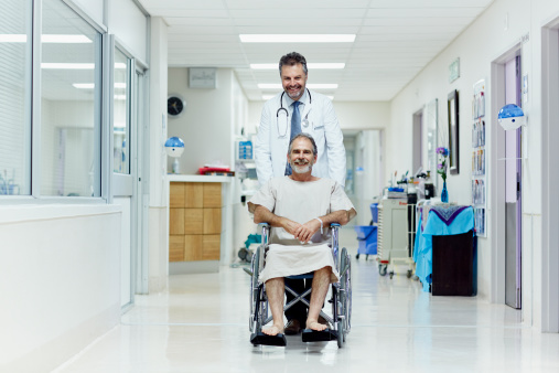 Happy doctor pushing disabled man in wheelchair at hospital corridor