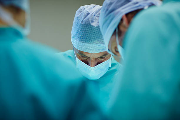 surgeons working in operating room - medizinischer vorgang stock-fotos und bilder