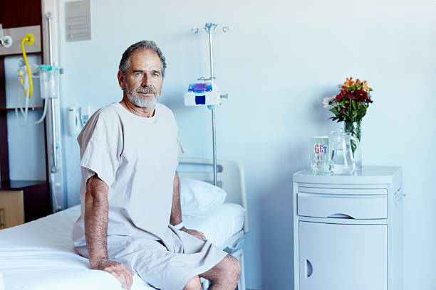Mature man in hospital ward Portrait of mature man sitting on bed in hospital ward three quarter length stock pictures, royalty-free photos & images