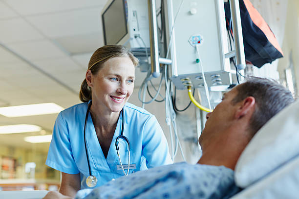 Smiling doctor looking at patient in hospital ward Happy female doctor looking at male patient lying in hospital ward hospital room stock pictures, royalty-free photos & images