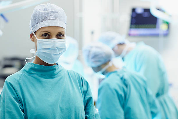 Portrait of confident female surgeon Portrait of confident female surgeon with colleagues working in operating room surgeon stock pictures, royalty-free photos & images